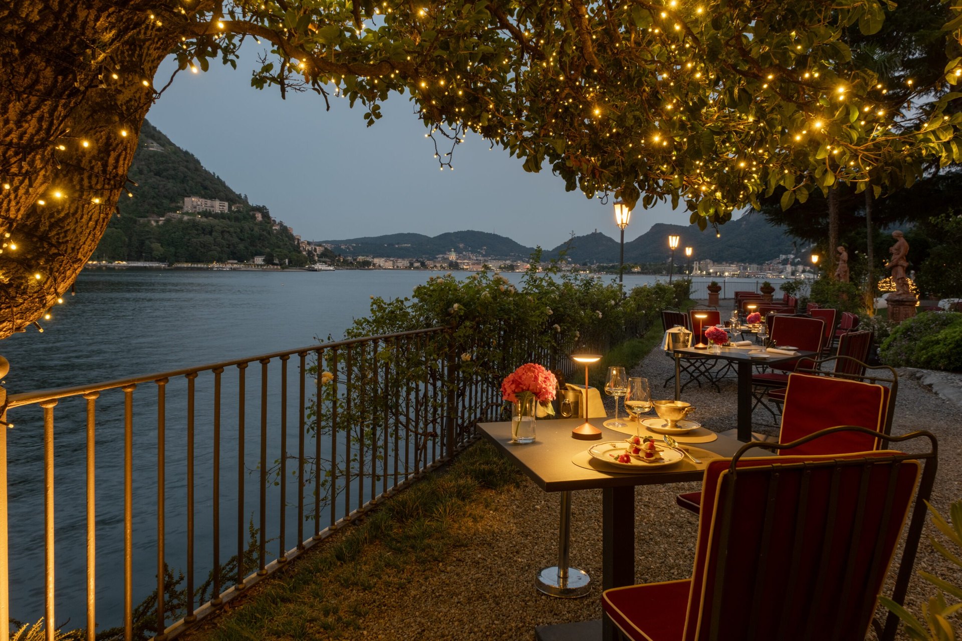 The garden terrace of the Ristorante Raimondi at Villa Flori at dusk, under a tree hung with lights, with Como across the water