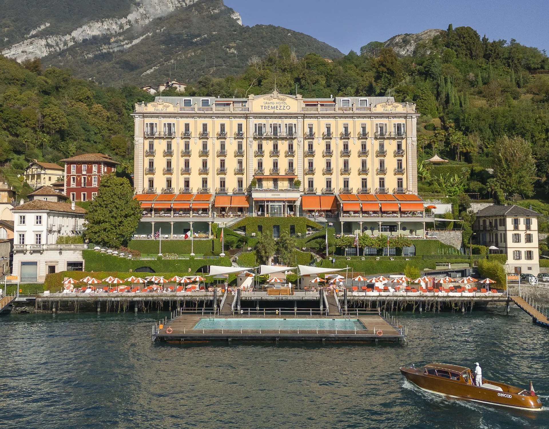 The Grand Hotel Tremezzo above its floating pool and lakeside terrace, with a wooden launch passing
