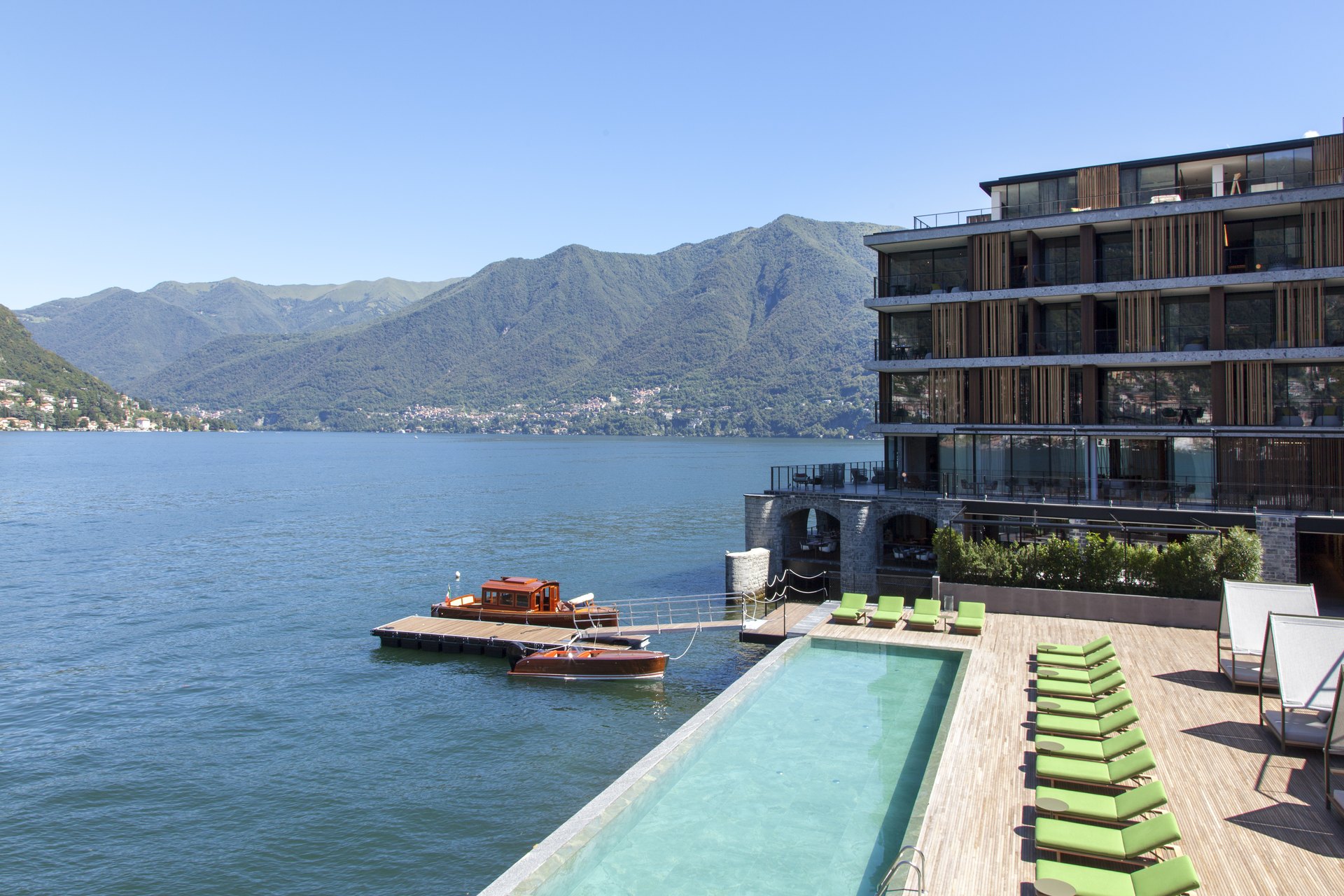 The lakeside pool and boat dock of Il Sereno at Torno, with a wooden launch and the mountains of the western shore