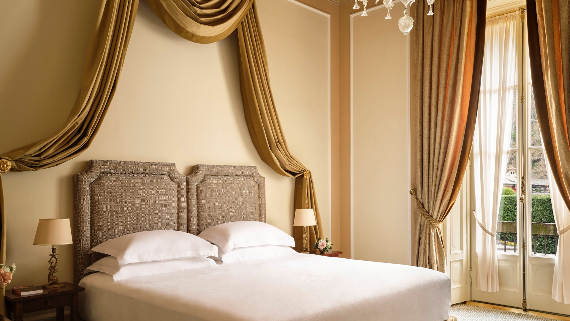 A room at Villa d’Este with a draped canopy over the bed and tall windows onto the garden