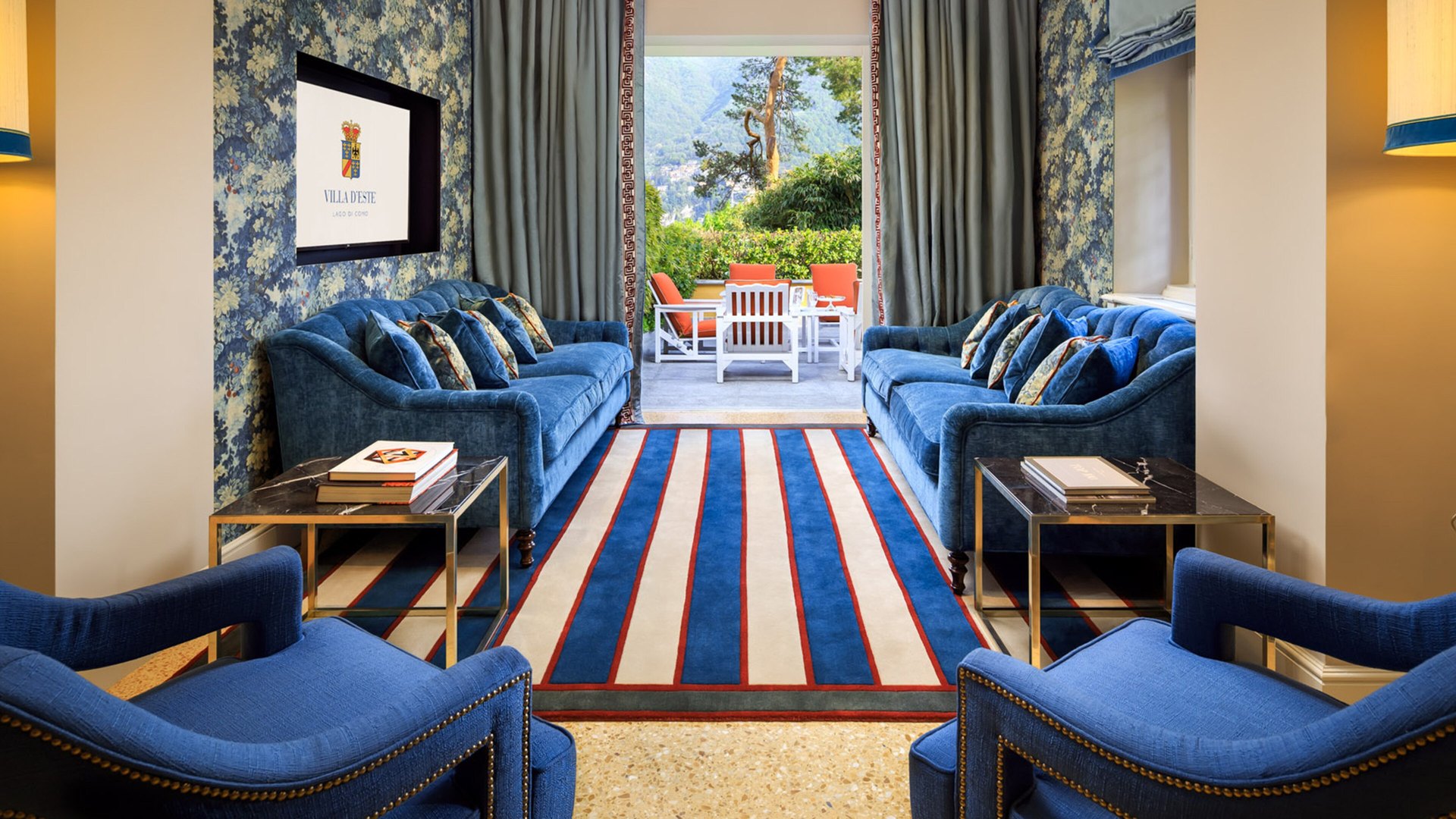 A sitting room in one of Villa d’Este’s villas: blue velvet sofas, a striped rug and doors open onto a garden terrace